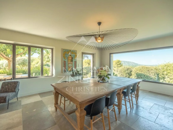 Interior of a Provençal house with a large wooden table and windows offering a view of the landscape.