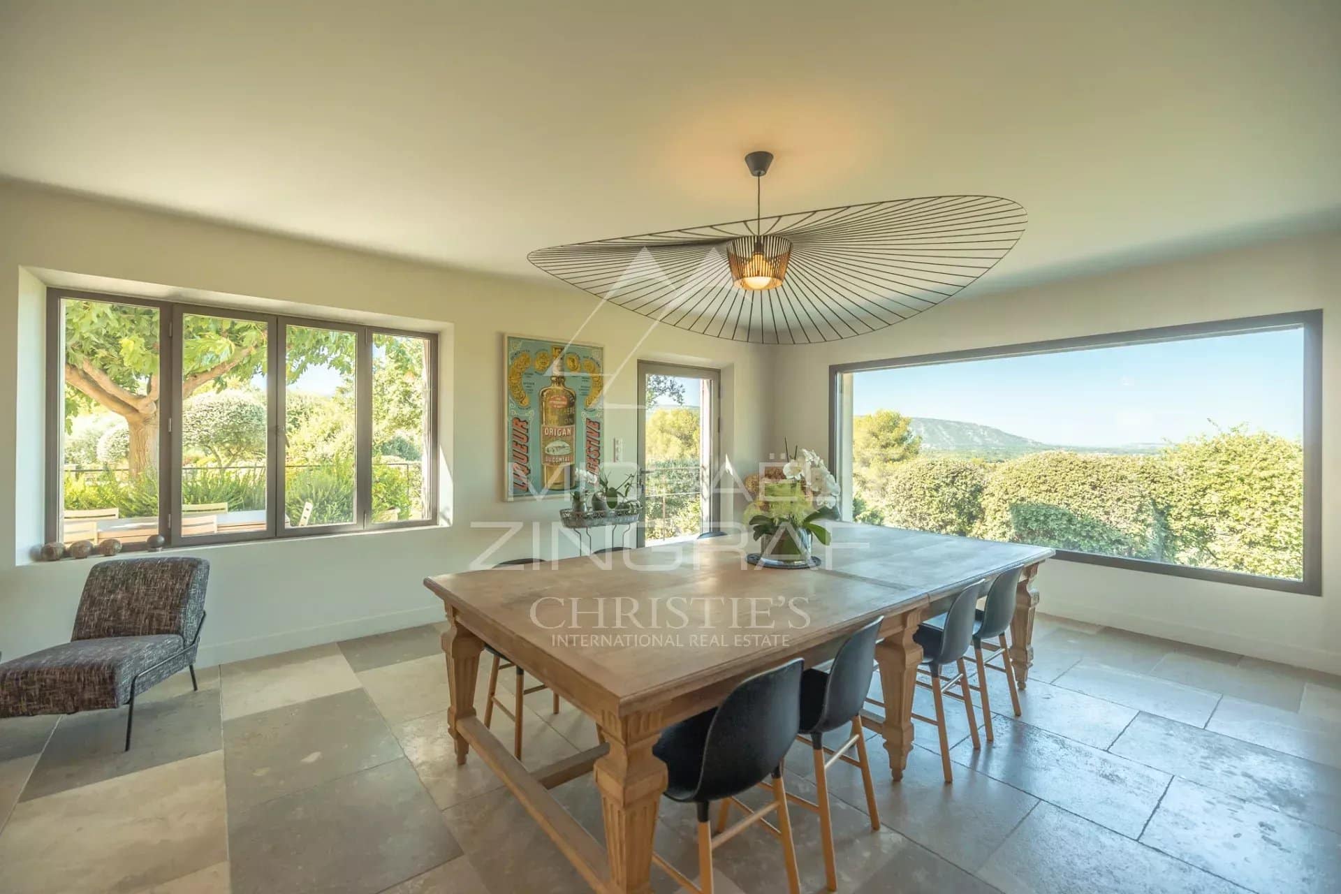 Interior of a Provençal house with a large wooden table and windows offering a view of the landscape.