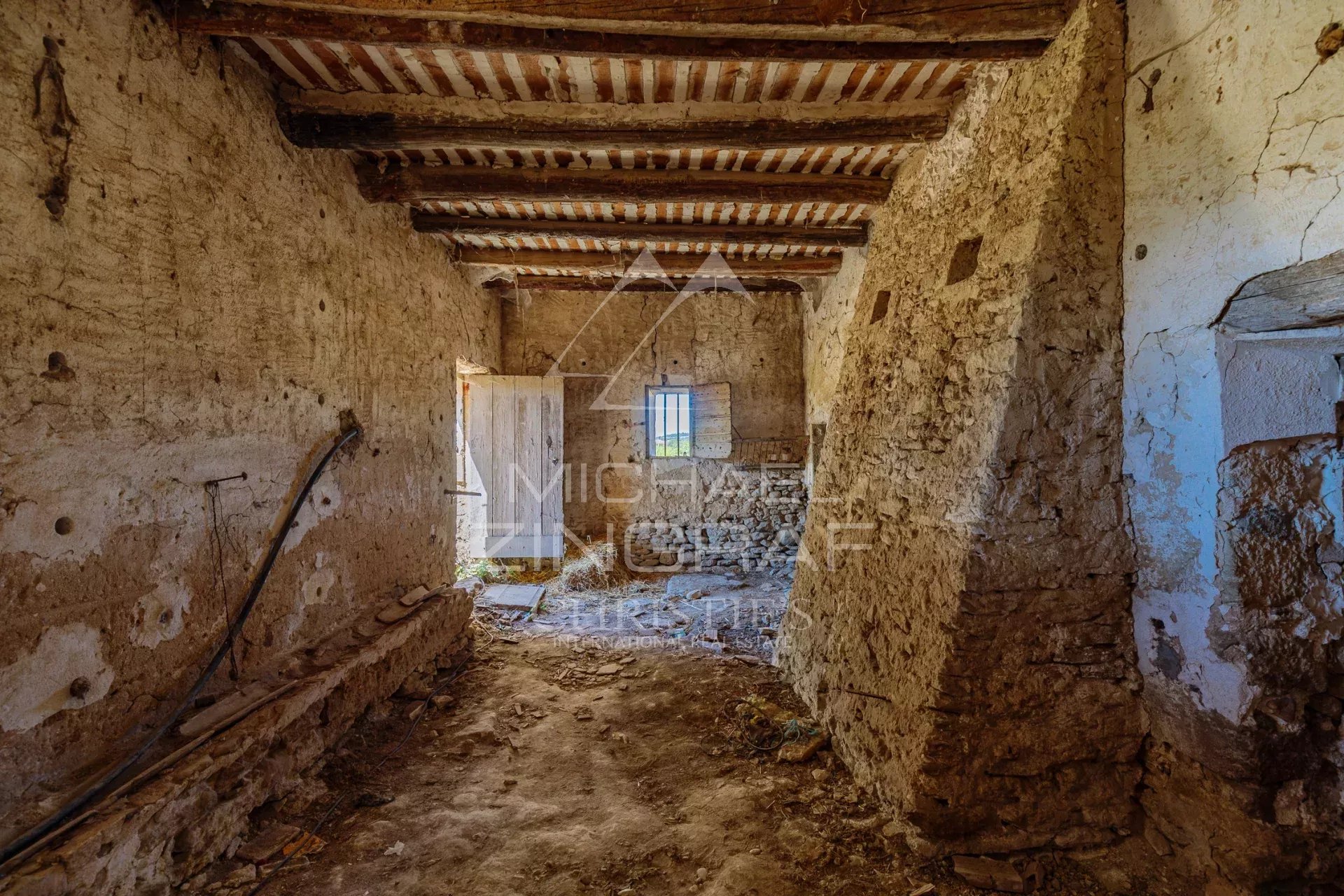 Intérieur d'un mas XVIIIe à rénover avec murs en pierre et poutres apparentes.