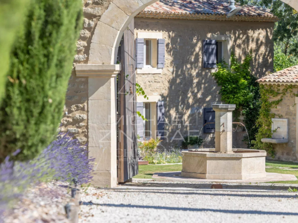 Entrance to a renovated farmhouse with a well, surrounded by gardens and trees, in Oppède.