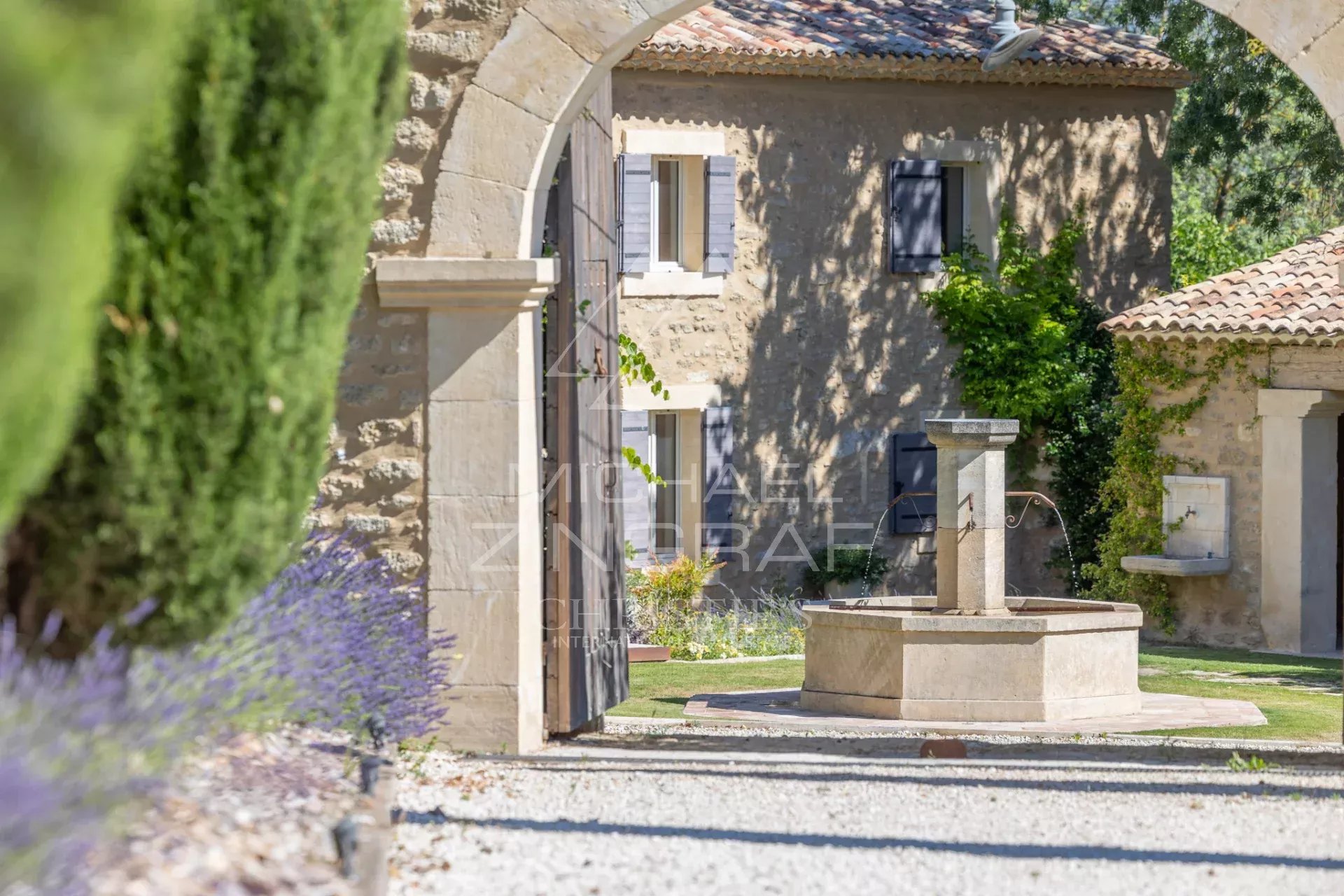 Renovated farmhouse in Oppède Entrance to a renovated farmhouse with a well, surrounded by gardens and trees, in Oppède.