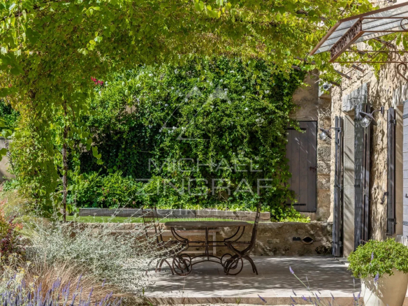 Terrace of a renovated farmhouse with table and chairs, surrounded by greenery in Oppède.