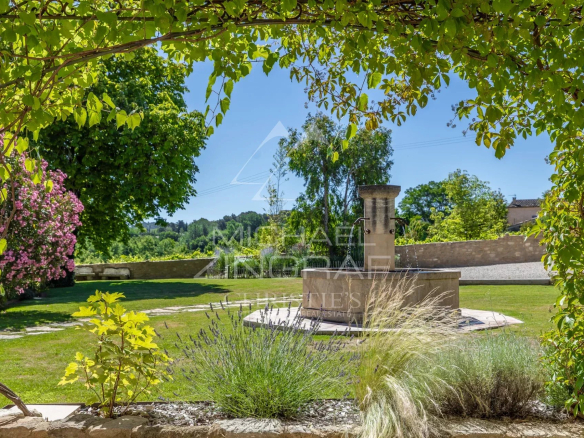 Garden of a renovated farmhouse in Oppède with a fountain and Mediterranean plants.