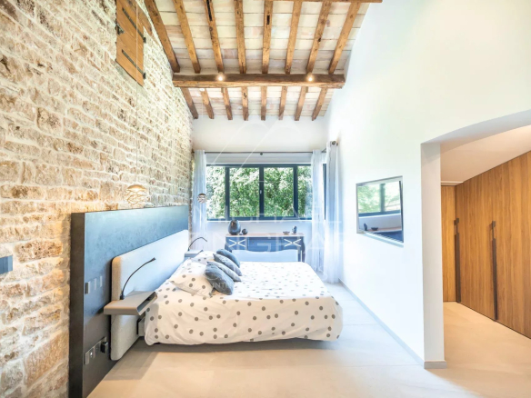 Modern bedroom with stone walls and wooden ceiling in a renovated property near L'Isle-sur-la-Sorgue.
