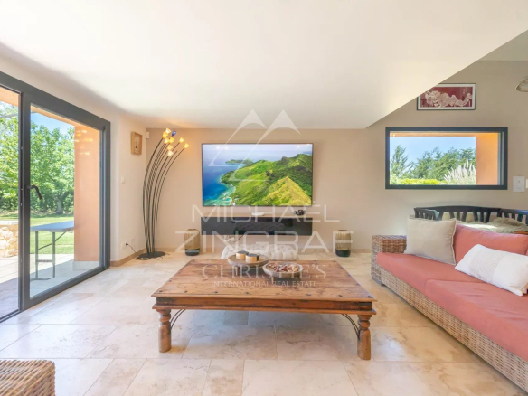 Intérieur d'un mas en pierre avec salon lumineux et télévision, vue sur jardin.