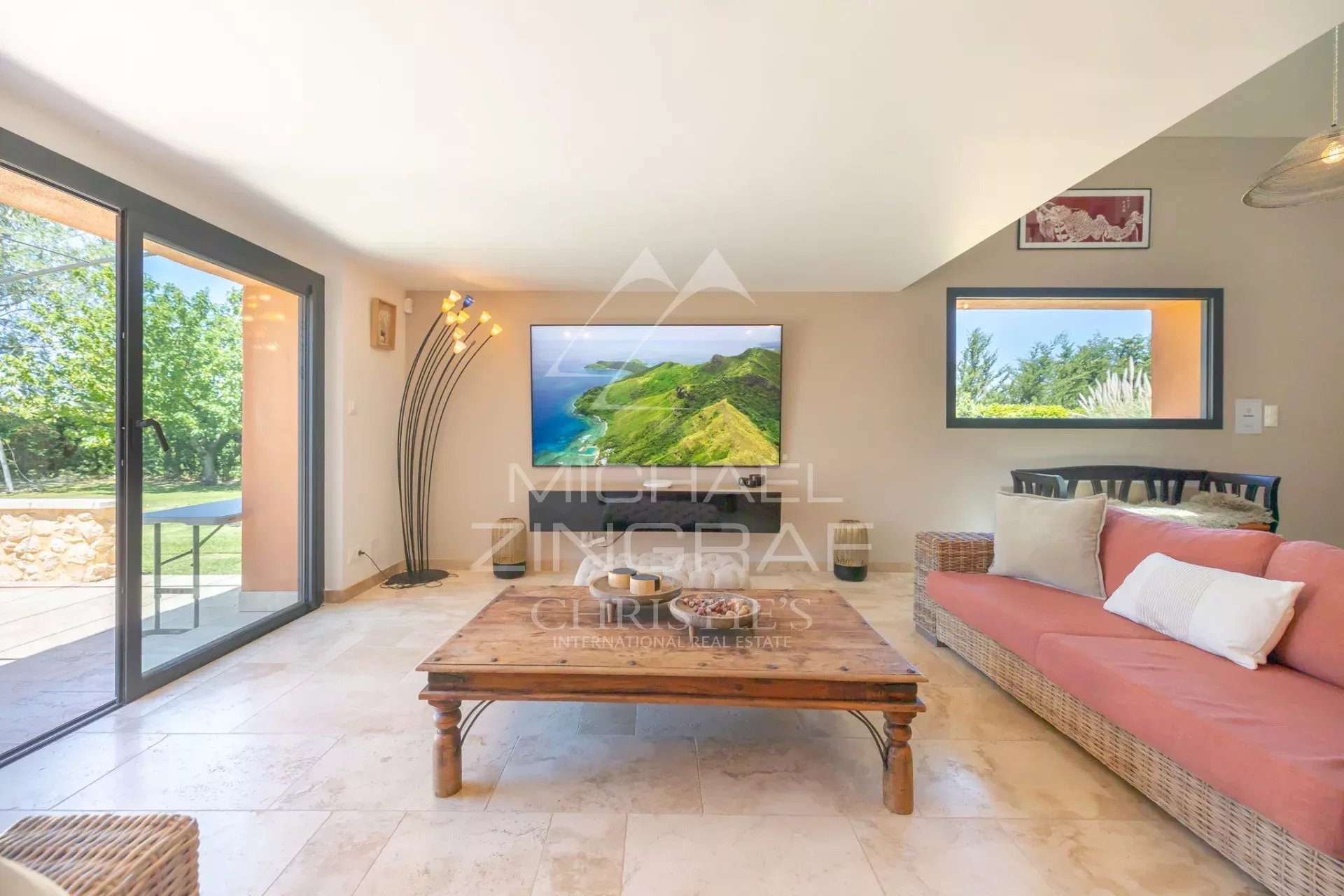 Intérieur d'un mas en pierre avec salon lumineux et télévision, vue sur jardin.