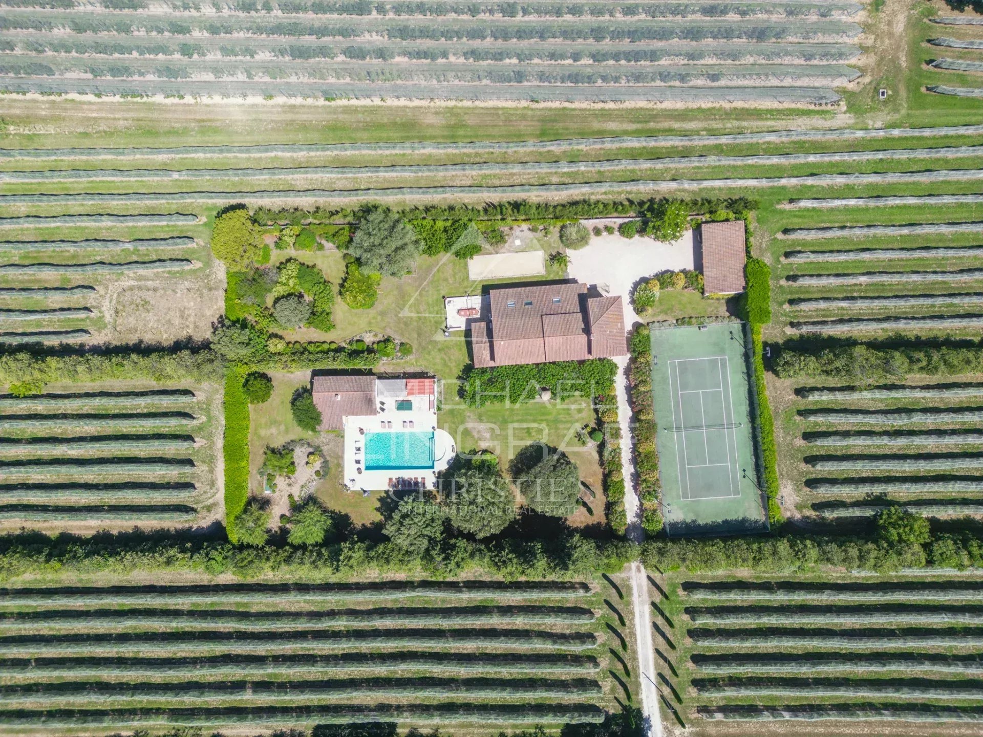 Vue aérienne d'un mas en pierre avec piscine et court de tennis entouré de jardins et de vergers à Cavaillon.