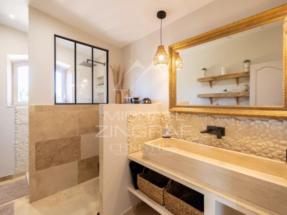 Salle de bain moderne avec lavabo en pierre et douche en verre, décorée de mosaïque et de lumière naturelle.