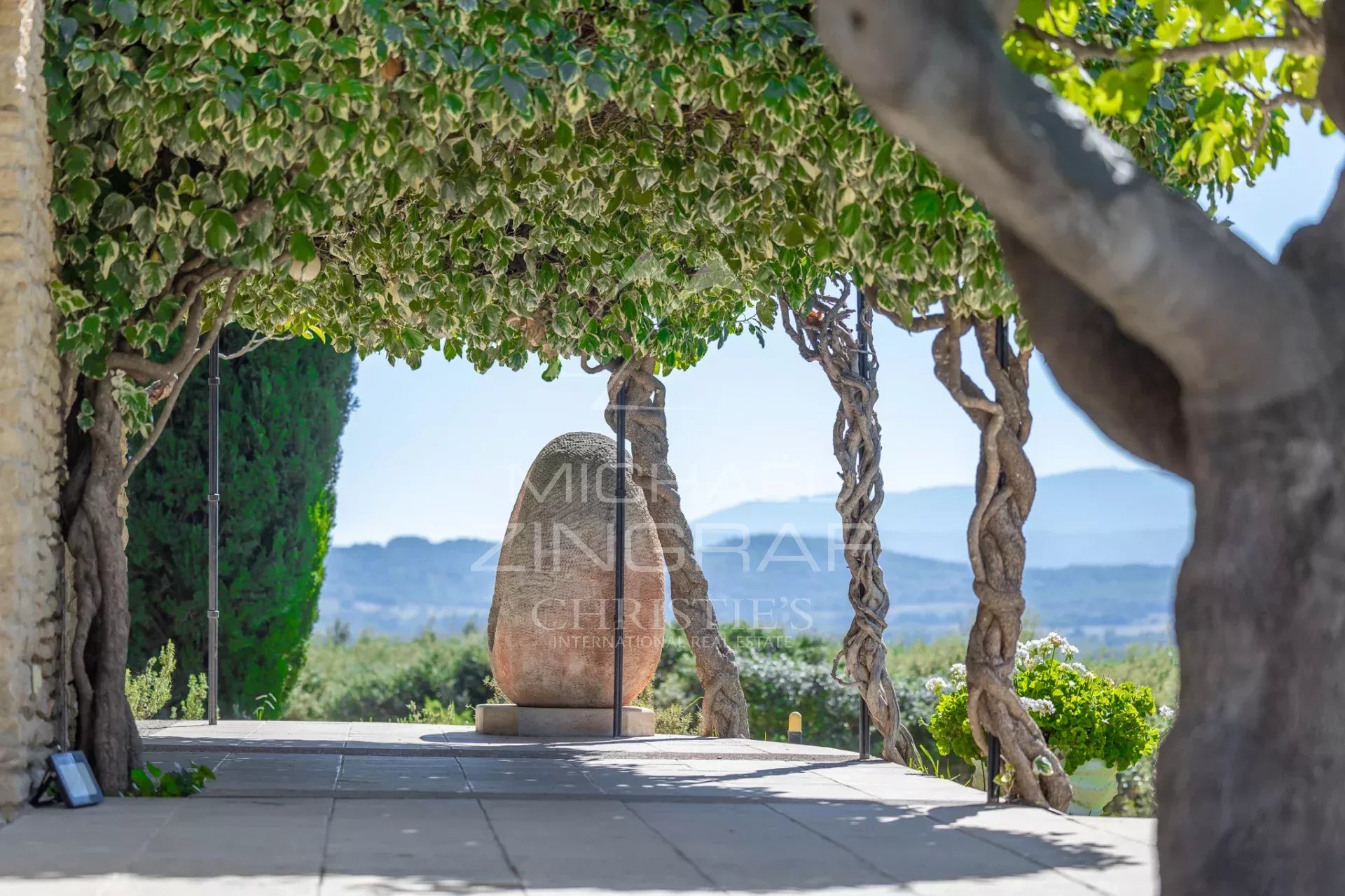 Maison d’architecte à Gordes Terrasse d'une maison d'architecte à Gordes, avec vue sur le paysage du Luberon et sculpture en pierre.