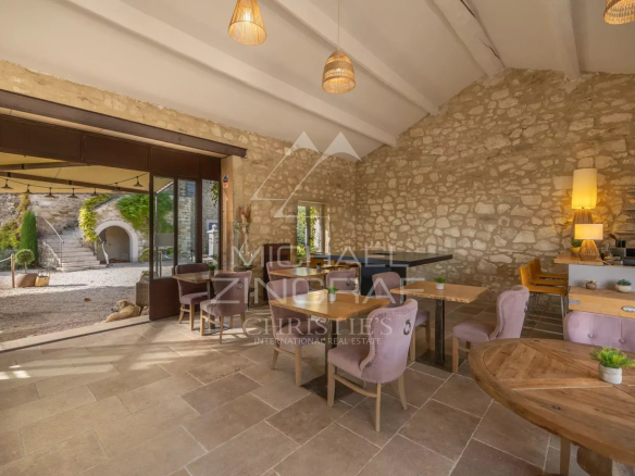 Interior of a Provençal farmhouse with tables and chairs, stone walls, and large bay windows.