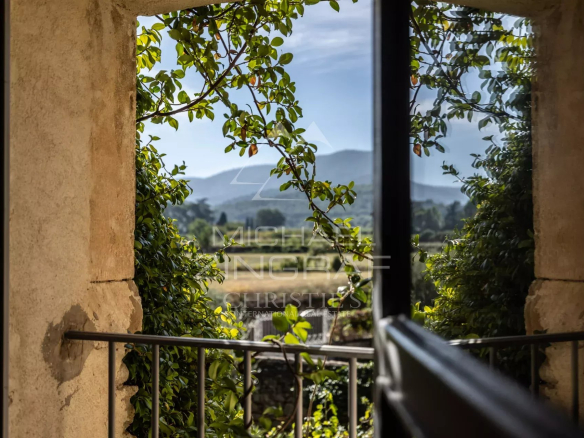 View from a window framed by greenery, showing the Luberon landscape.