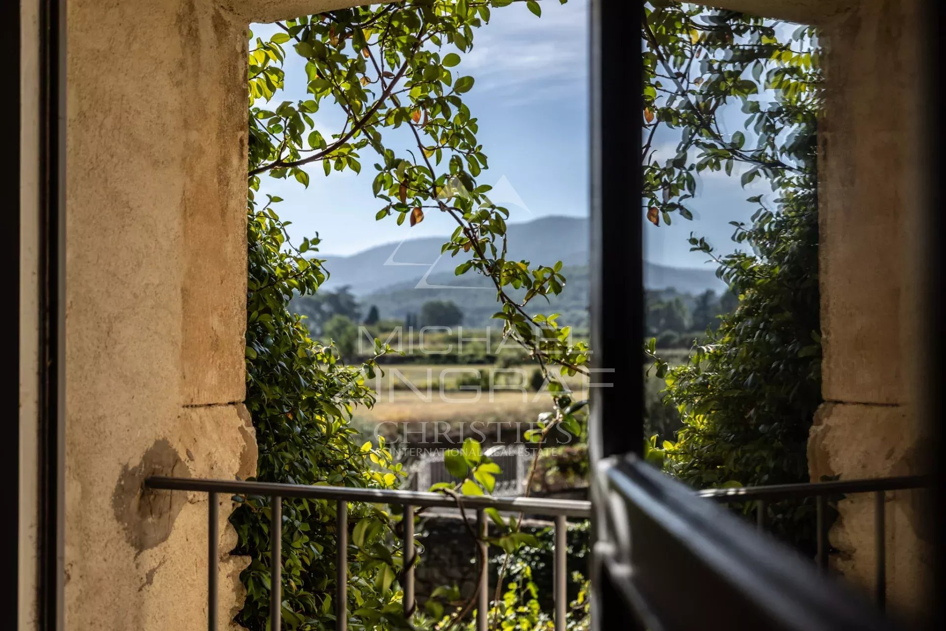 View of the Luberon from a window View from a window framed by greenery, showing the Luberon landscape.