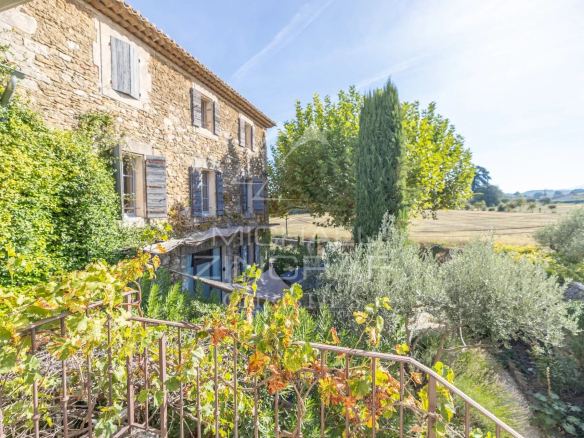 Provençal stone farmhouse with gîtes and guest rooms in Oppède, surrounded by greenery and fields.