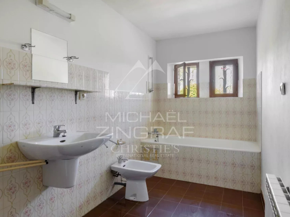 Bathroom in a house to be renovated, with sink and toilet, tiled walls.