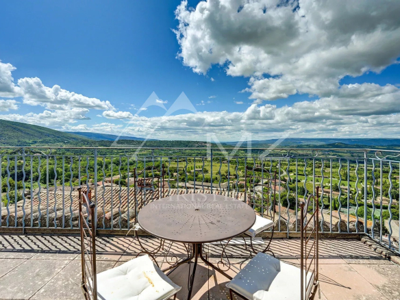 Vue panoramique depuis une terrasse avec table et chaises, sur le Luberon à Bonnieux.