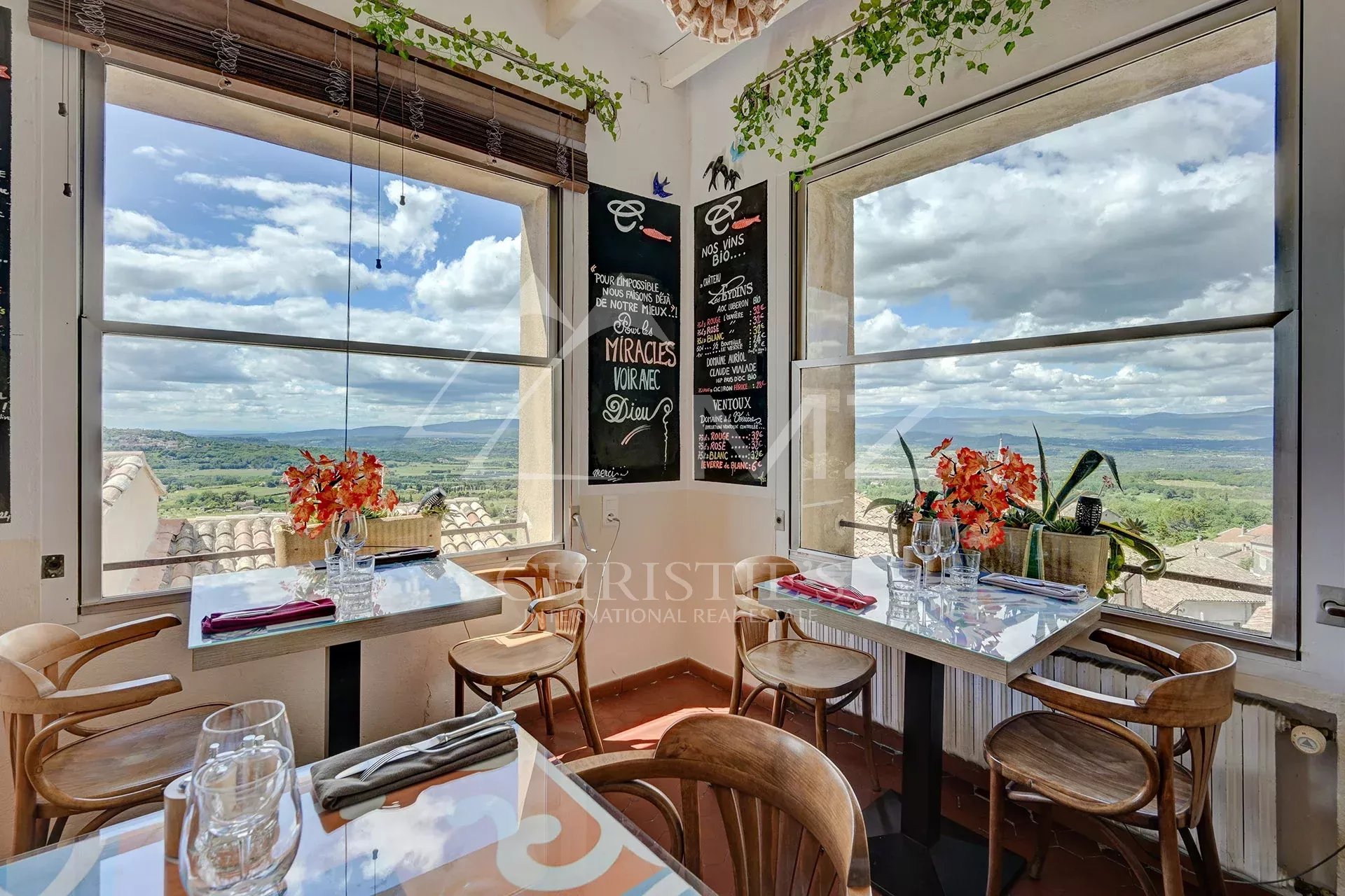 Restaurant avec vue sur le Luberon Intérieur d'un restaurant avec vue panoramique sur le Luberon, tables décorées et plantes.