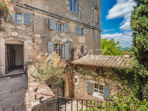 Entrance to a stone building with shuttered windows, surrounded by greenery in Ménerbes.