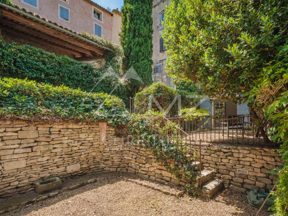Garden and access to a characterful building in Ménerbes, with stone walls and green plants.