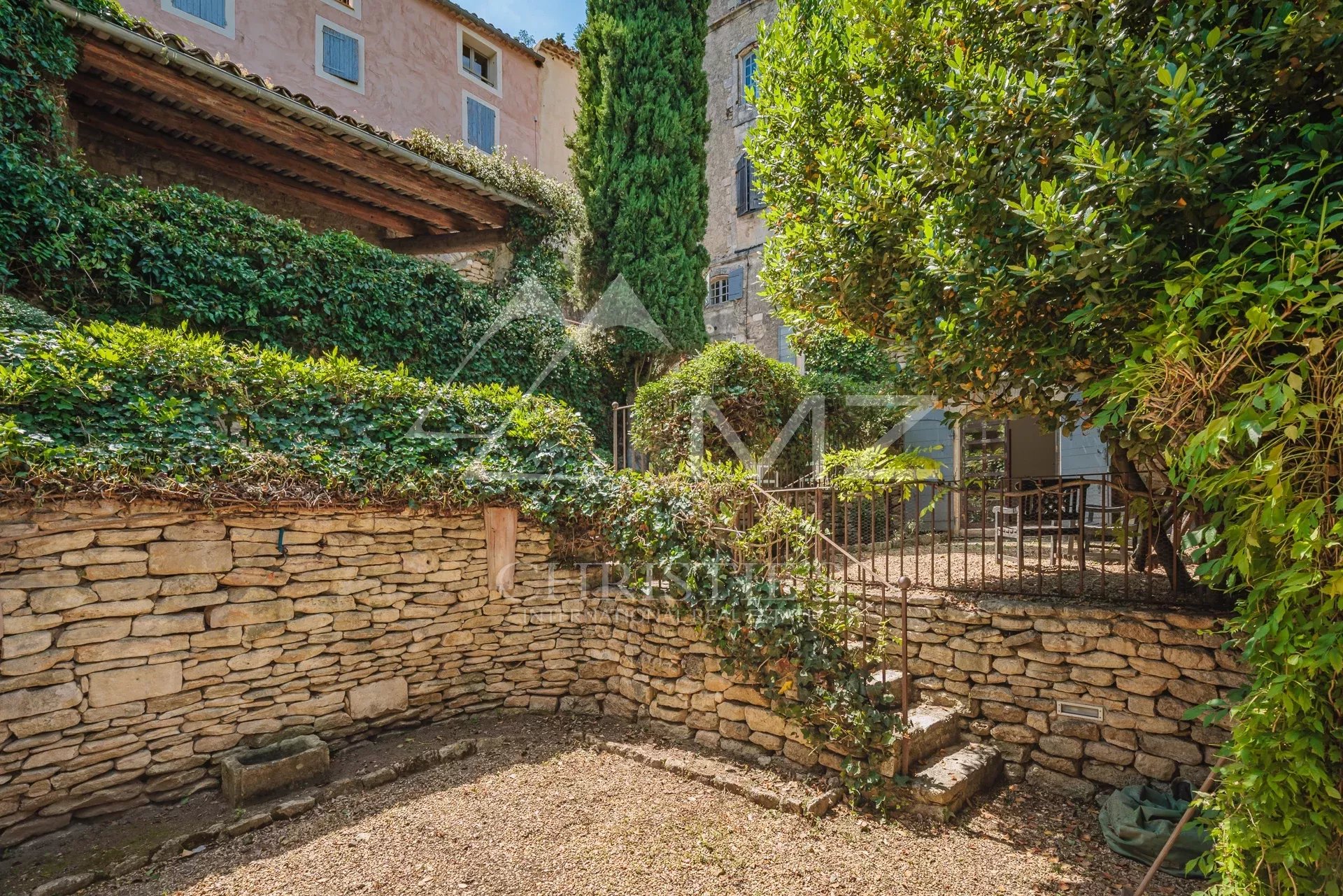 Garden and access to a characterful building in Ménerbes, with stone walls and green plants.