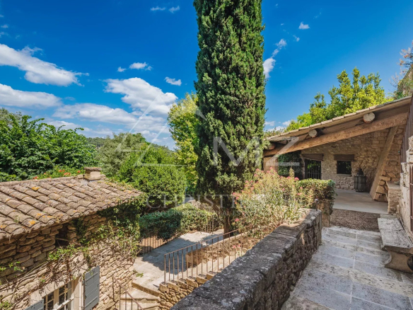 Exterior view of a stone building with a garden in Ménerbes under a blue sky.