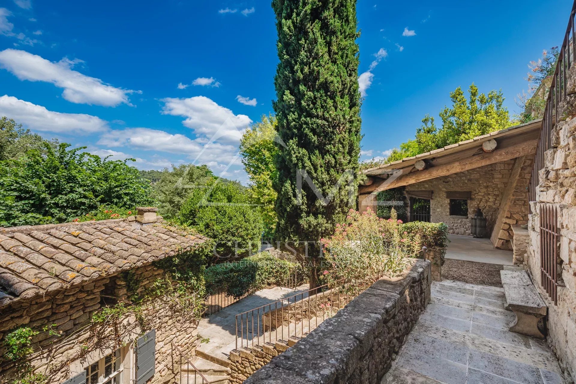 Exterior view of a stone building with a garden in Ménerbes under a blue sky.