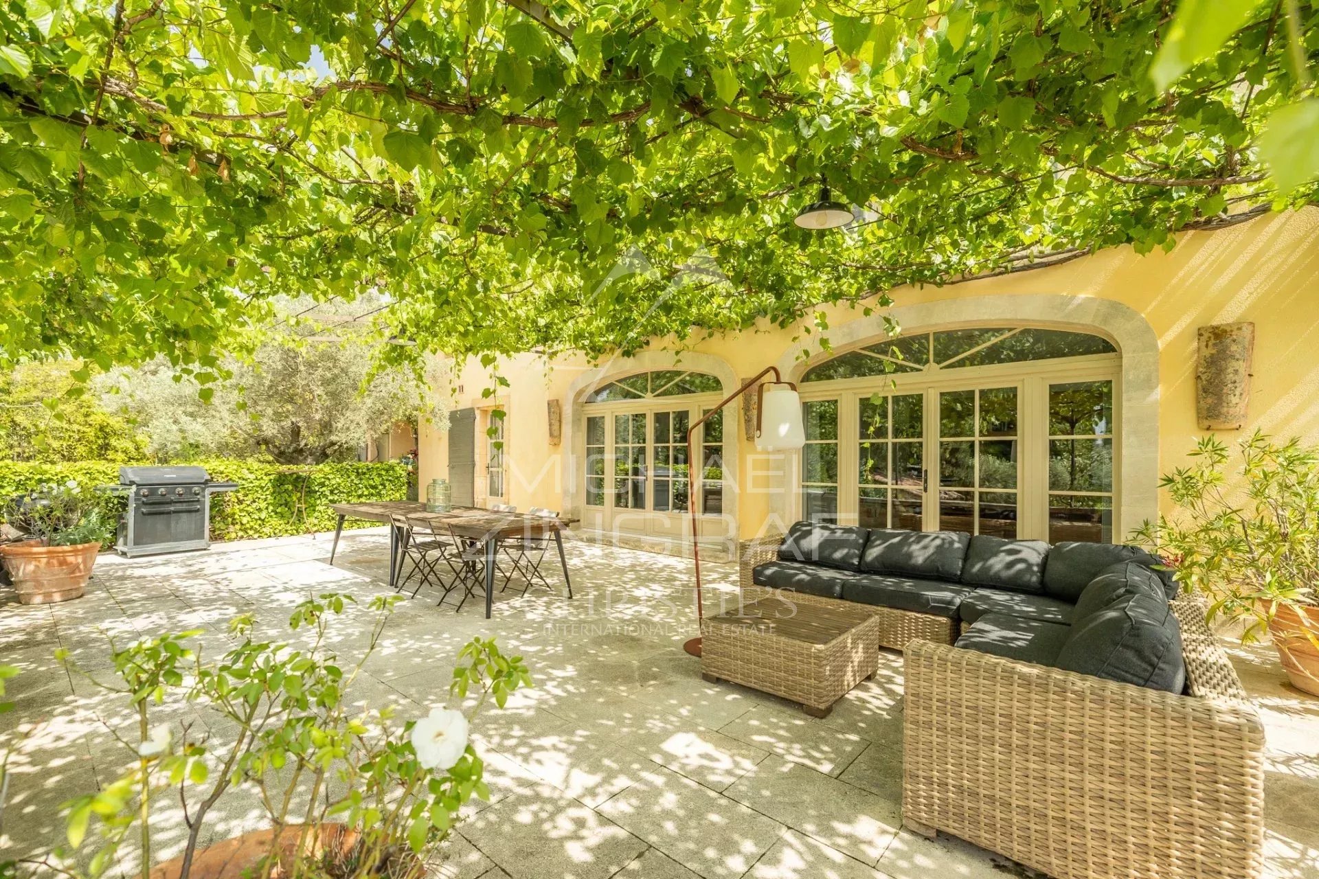 Terrasse d’une propriété à Saint-Saturnin-lès-Apt Terrasse ombragée d'une propriété provençale avec mobilier en osier et barbecue.