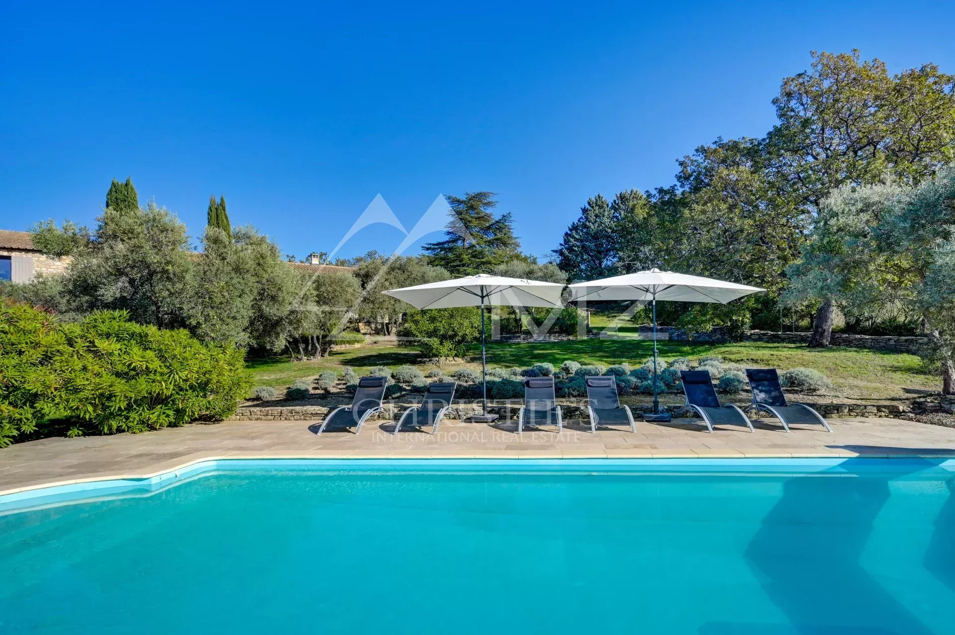 Piscine et jardin à Gordes Piscine avec chaises longues et parasols dans un jardin ensoleillé à Gordes.
