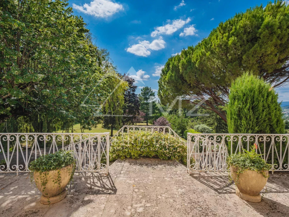 Terrasse d'une maison avec vue sur un parc paysagé, arbres et ciel bleu.