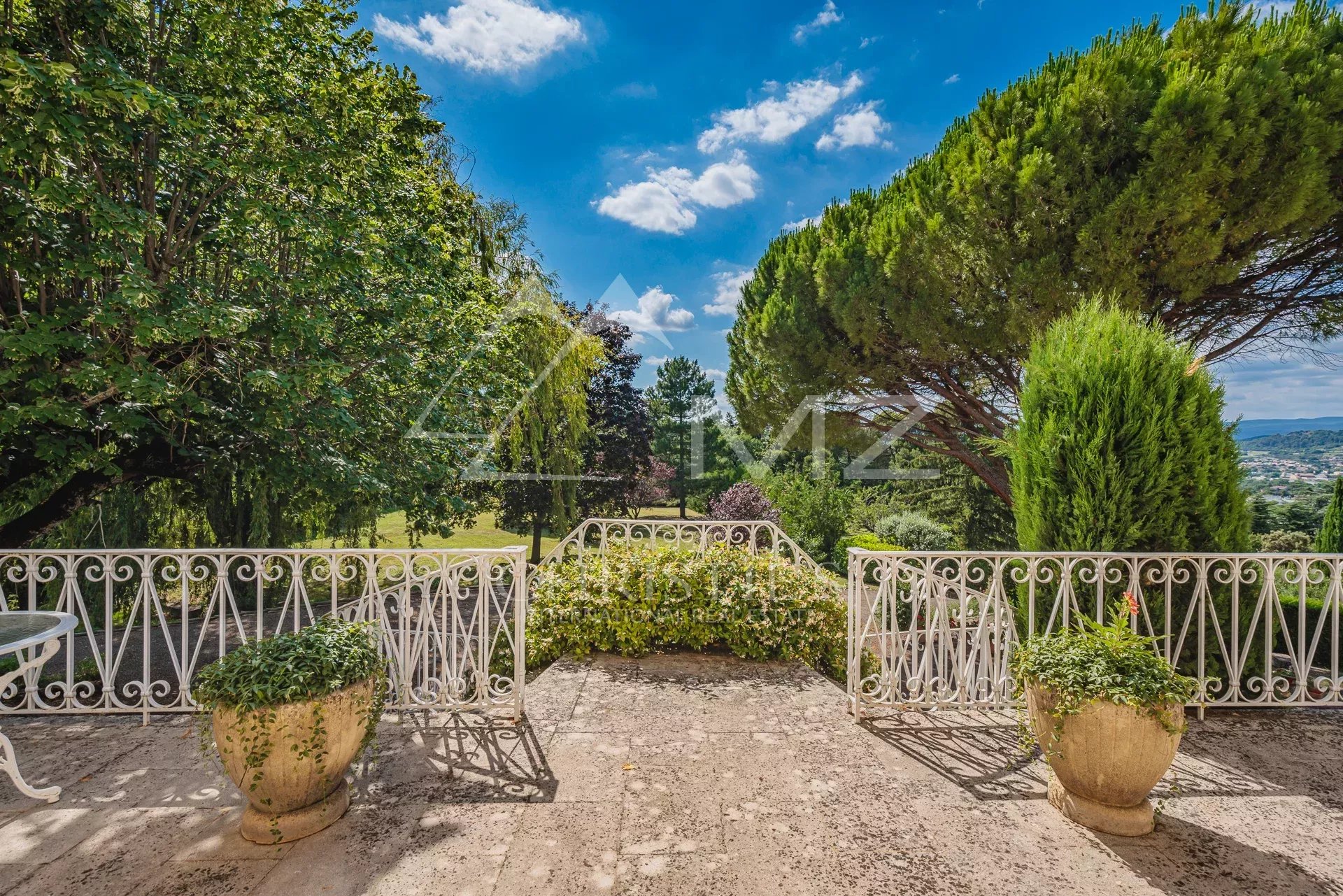 Terrasse avec vue sur le parc Terrasse d'une maison avec vue sur un parc paysagé, arbres et ciel bleu.