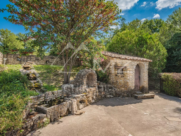 Bâtiment en pierre dans un parc paysagé avec arbres et verdure, près d'Apt.