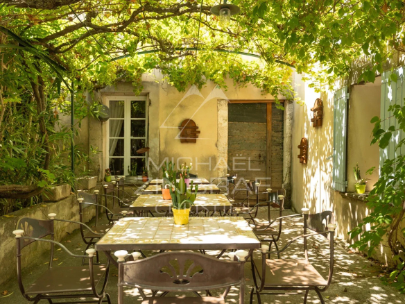 Terrasse ombragée avec tables et chaises, entourée de verdure dans un ancien prieuré.