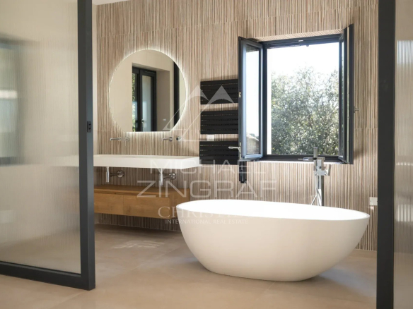 Modern bathroom with freestanding bathtub and window offering a view of nature.