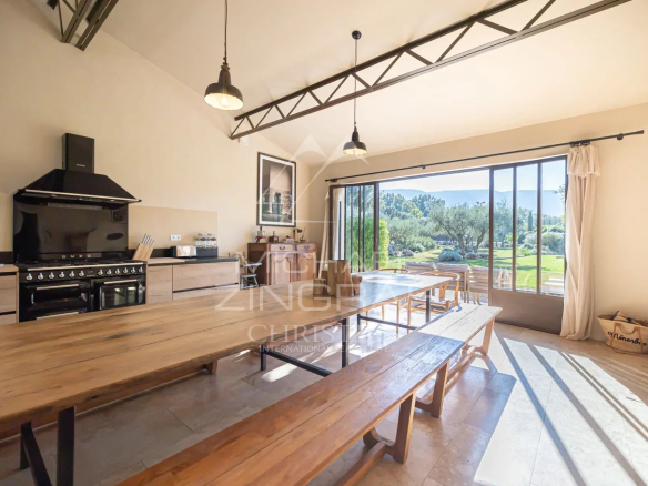 Interior of a Provençal country house with large windows and a view of a landscaped garden.