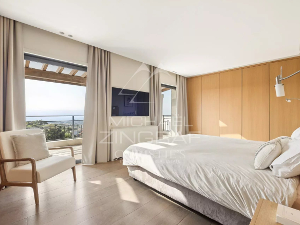 Bright hotel bedroom with a king bed, wooden wardrobe, and a balcony overlooking the sea from the window.