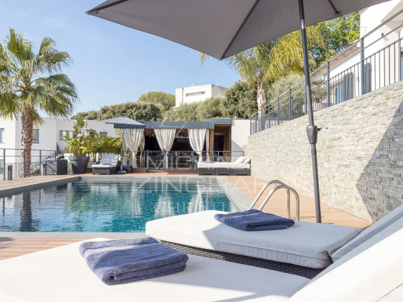Poolside deck with white loungers, blue towels, and a large umbrella overlooking a rectangular pool and cabana.