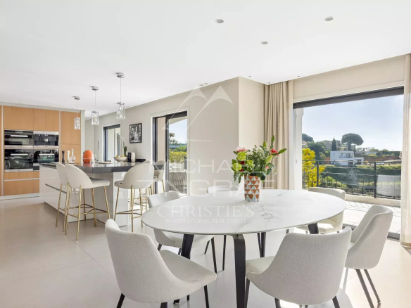 Bright open-plan kitchen and dining area with a round marble table, white chairs, and large windows leading to a balcony view.