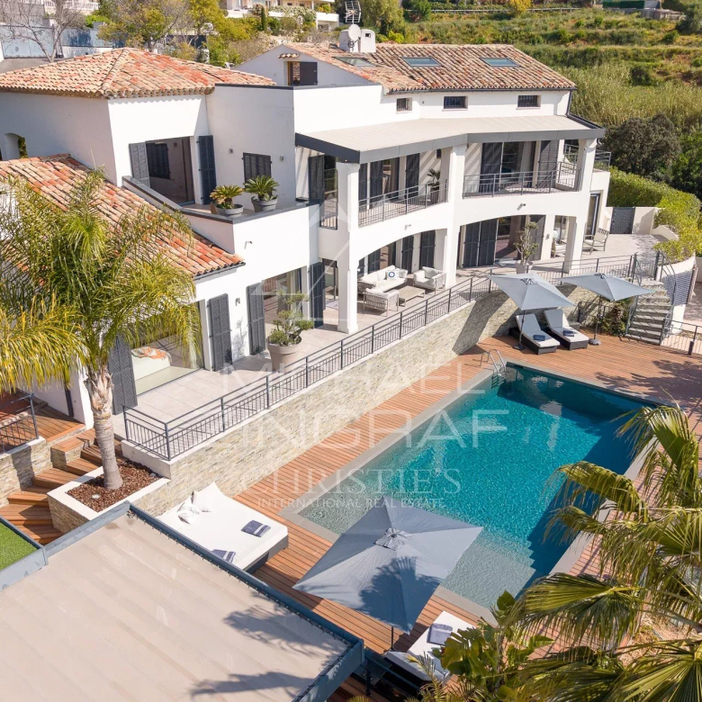 Modern white villa with red-tiled roofs, terraces, and a large rectangular pool with sun loungers.