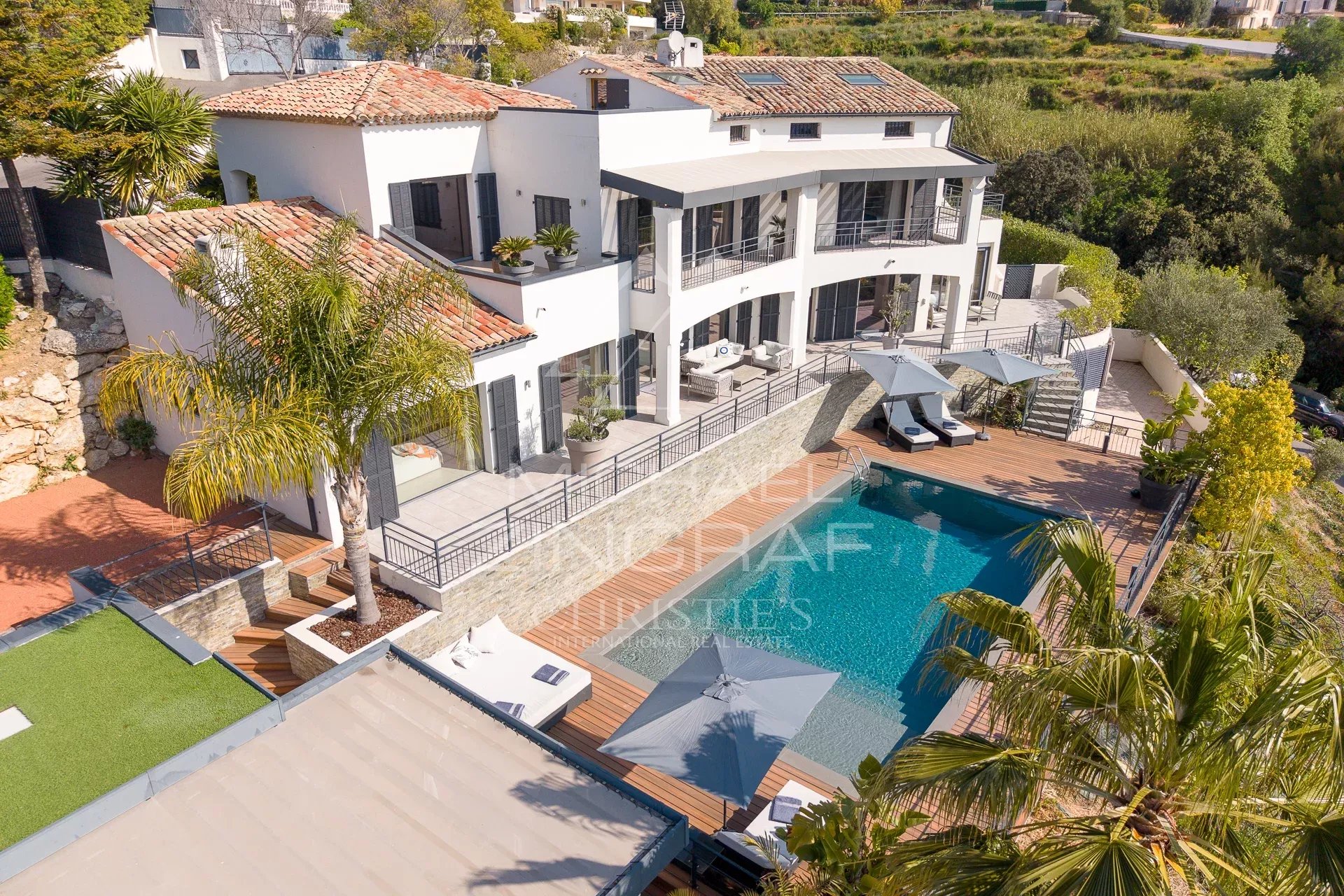 Modern white villa with red-tiled roofs, terraces, and a large rectangular pool with sun loungers.