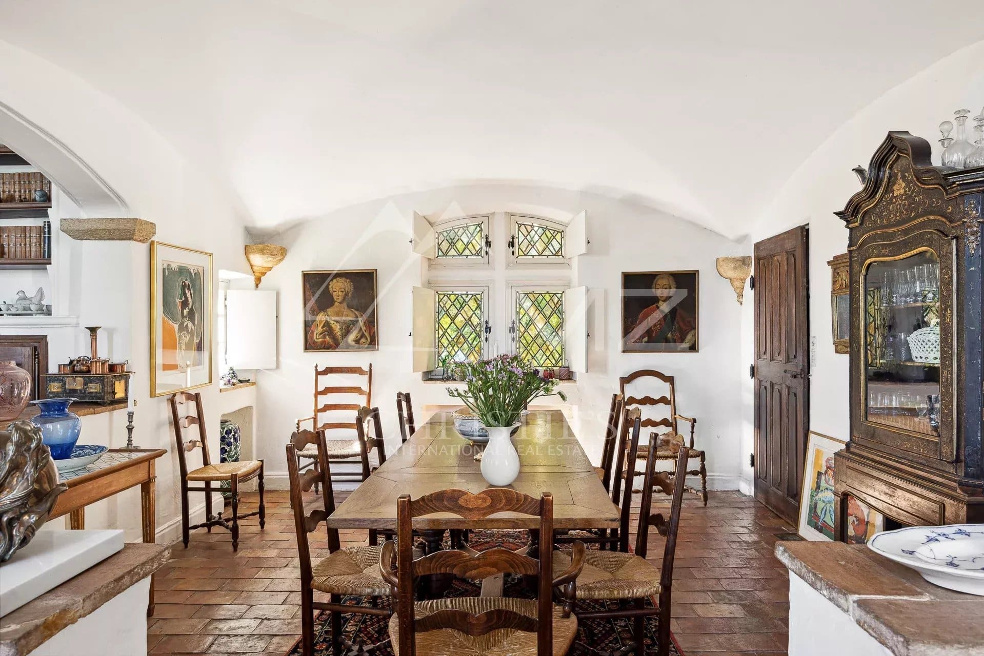 Dining room of a manor house in Tourrettes-sur-Loup with wooden chairs and paintings on the walls.