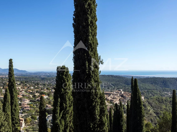 Panoramic view of Tourrettes-sur-Loup and the sea from a property with cypress trees.