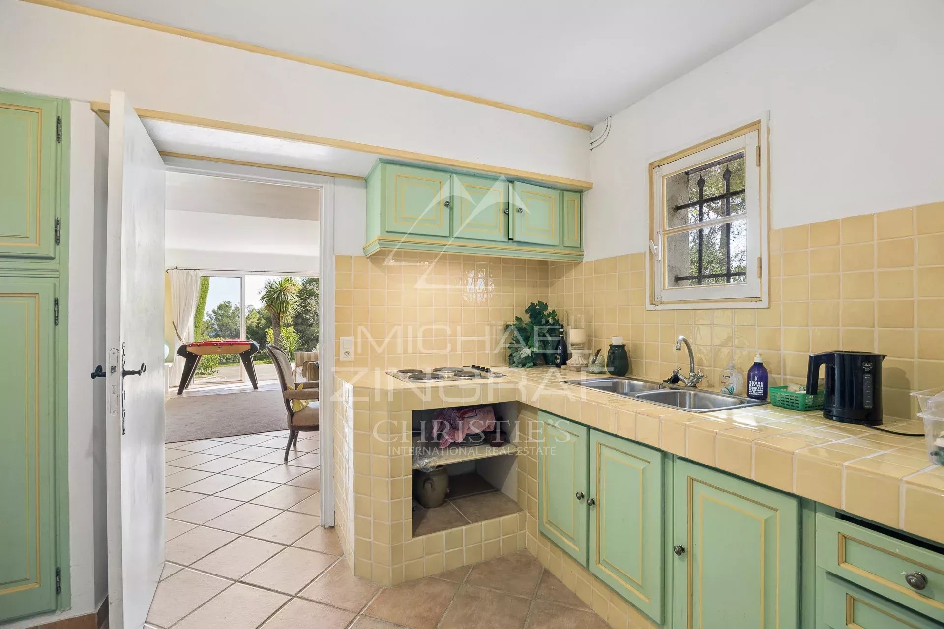 Kitchen of a villa in Saint-Paul-de-Vence Kitchen of a villa with beige tiles and green furniture, overlooking a bright living space.