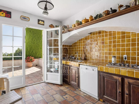 Bright kitchen with terracotta tiles and wooden furniture, opening onto an outdoor space.