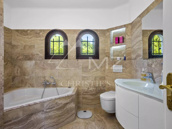 Modern bathroom with bathtub and sink, beige stone walls, arched windows.