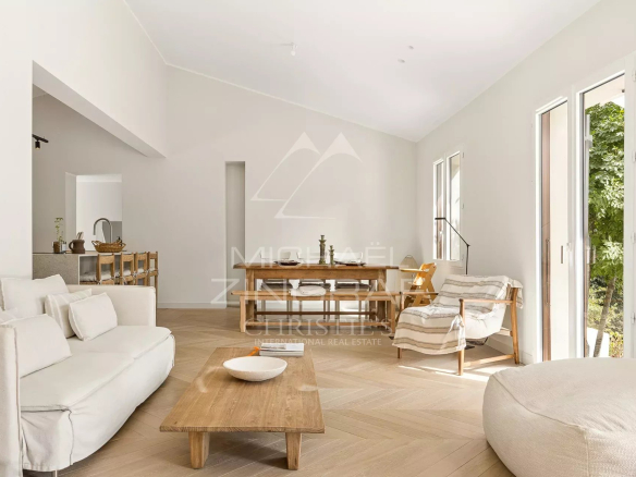 Intérieur d'une villa rénovée avec un salon lumineux et des grandes fenêtres donnant sur un parc.