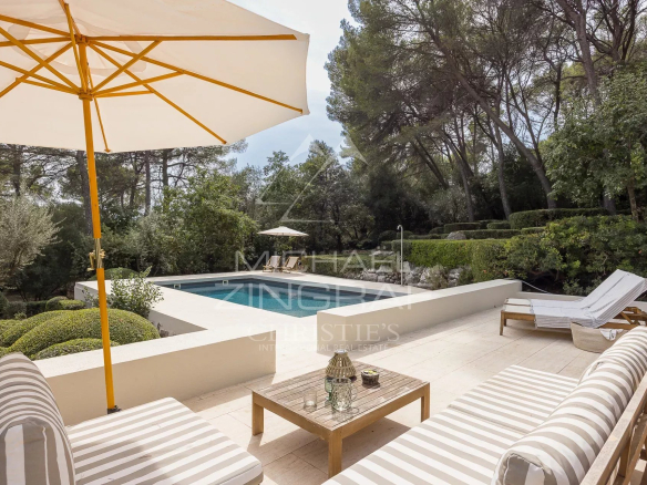 Terrasse d'une villa rénovée avec piscine, chaises longues et parasol, entourée de verdure.