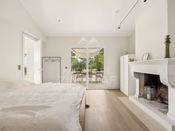 Chambre d'une villa rénovée avec cheminée et accès à l'extérieur, située dans un parc paysager.