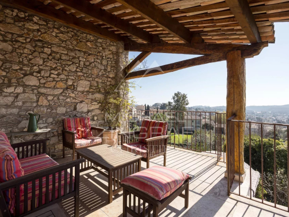Terrasse ensoleillée avec mobilier en bois et vue sur le village de La Colle-sur-Loup.