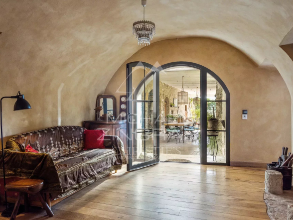 Intérieur d'une maison avec un salon au style ancien et une porte vitrée donnant sur un espace lumineux.