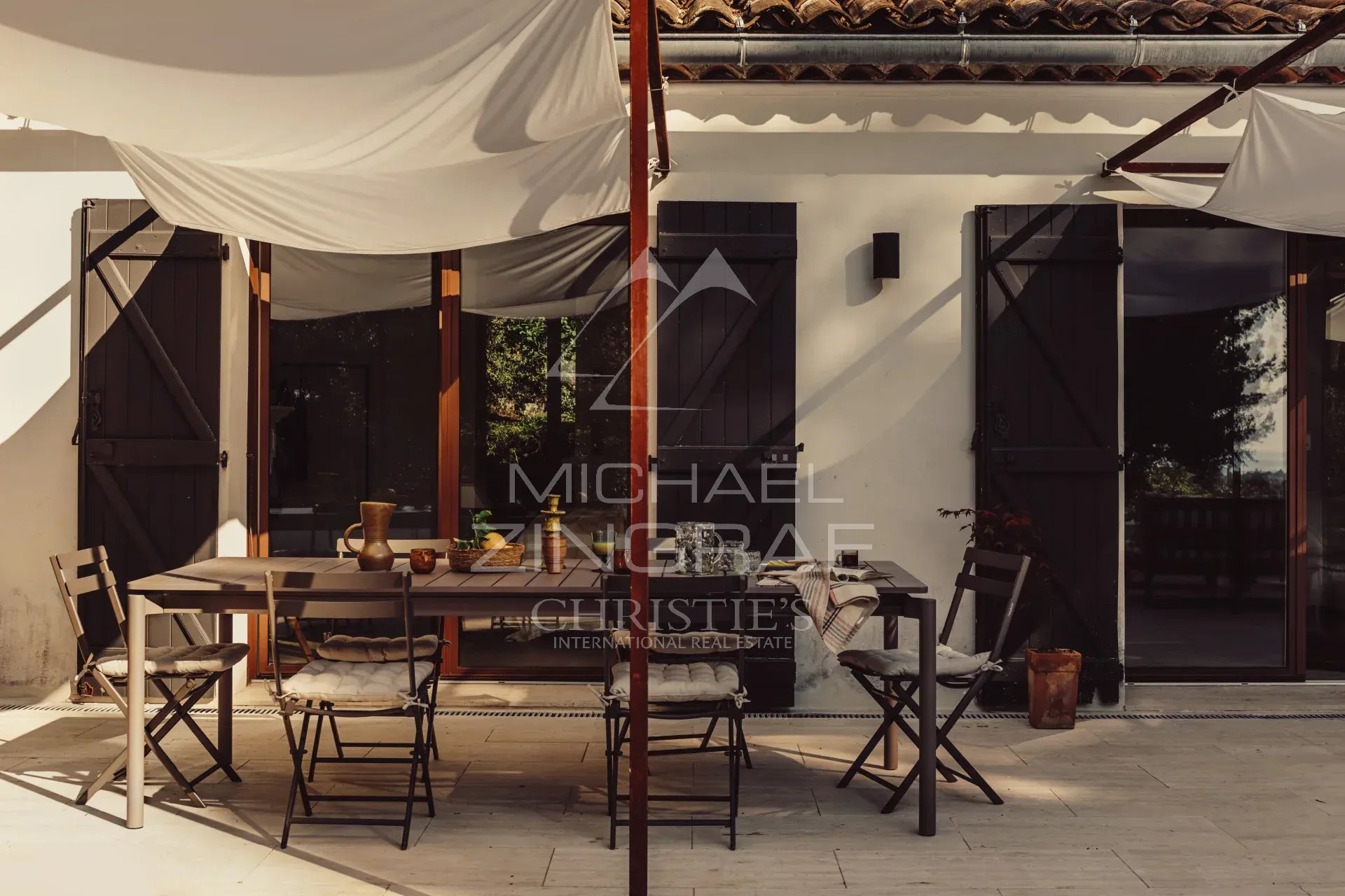 Terrace of a renovated villa Terrace of a renovated property with wooden furniture and chairs, surrounded by greenery.