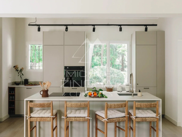Modern kitchen with central island and bar, overlooking a landscaped park.